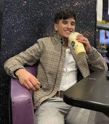 Devraj Jheet sitting in a purple seat, smiling and holding a drink in a cup.