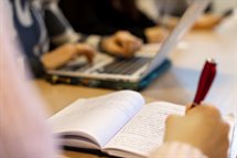 Students writing in a notebook and on a laptop.