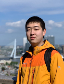 Lefan Wang wearing an orange jacket, standing in front of a blurred out city