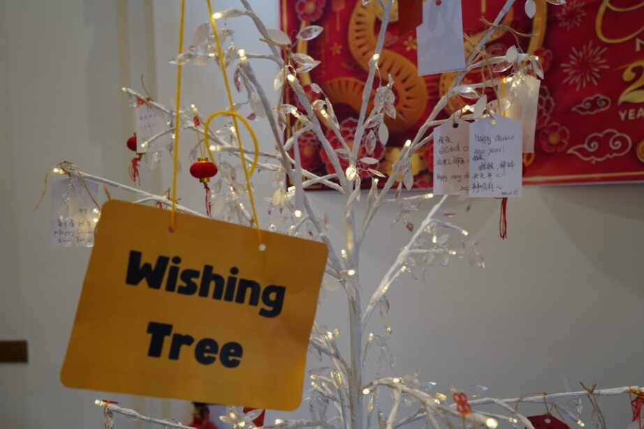 A sign reading "Wishing Tree" hanging from a white fake tree covered in lights.