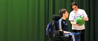 A person in a wheelchair and a person both looking at a ball