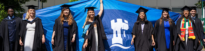 graduates in hats and gowns with university logo flag