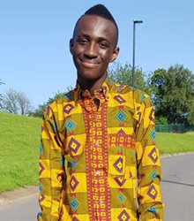 Francis Adam standing outside, wearing a patterned shirt and smiling to the camera