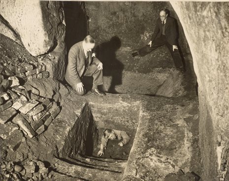 A black and white photograph of men in a cave, two on an upper level and one emerging from a lower level. Photo is from the Peverel Research Group Annual Report 1951.