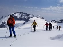 A group of warmly dressed people walking across a snowy landscape, attached to each other by ropes.