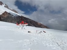 Red helicopter landing on a snowy landscape with a mountain in the background.