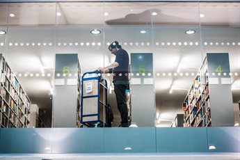 A floor length window above showing a staff member among rows of library shelves