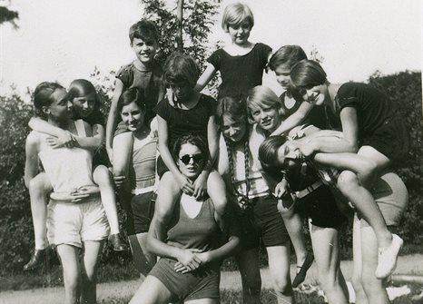 Black and white image of a large group of children and young people in shorts and t-shirts sitting on each others' shoulders to pose for the photo