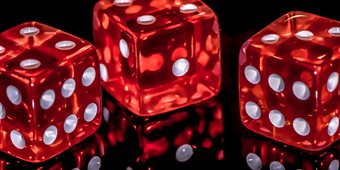 Three red dice with white spots on a black reflective surface