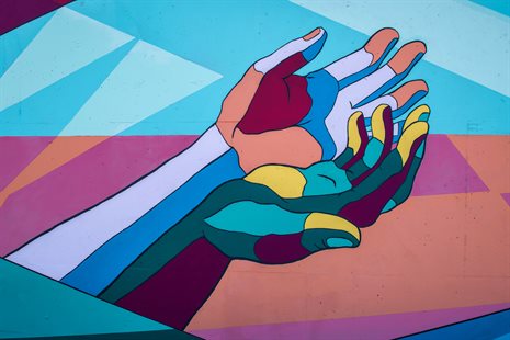A mural of cupped hands reaching out which is painted in abstract colours