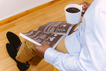 Photo of man reading booklet and holding a coffee
