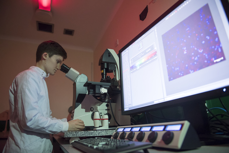 Student in a lab, looking into a microscope next to a computer screen