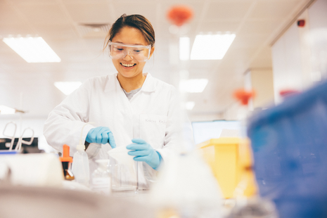 Smiling student working in a lab with goggles and gloves on