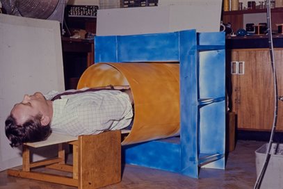 Colour photo of Peter Mansfield lying inside a mock-up of an MRI scanner.  This image is from the papers of Peter Mansfield, held by Manuscripts and Special Collections.  Document reference PPM/15/78/11.