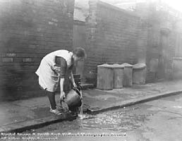 Woman collecting water from a communal water pump on Malt Mill Lane, Narrow Marsh area, 1931.