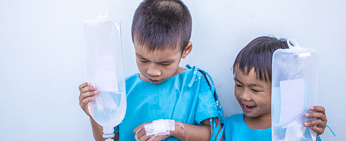 Two young boys in hospital gowns playing with IV drips
