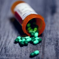 Green and turquoise pills falling out of an orange prescription bottle