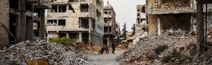 Image of two people crossing the street in a war-torn town