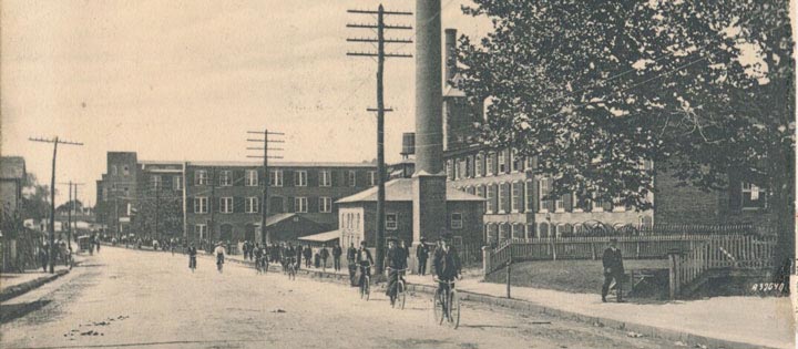 An old sepia postcard of lace workers cycling away from a lace factory in Patchogue, Long Island, New York State.
