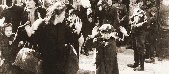 A black and white photo of a crowd of Jewish people with their hands up in the Warsaw Ghetto in May 1943