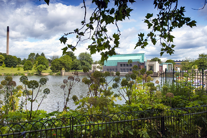 A colour photo of Highfields Lake with Lakeside Arts in the background and trees in the foreground.