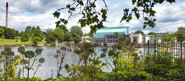 A colour photo of Highfields Lake with Lakeside Arts in the background and trees in the foreground.