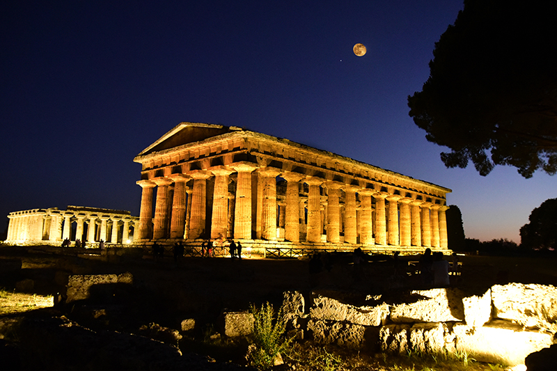A photo at night of the southern sanctuary temple at Paestum in southern Italy, the temple's columns lit up by floodlights.