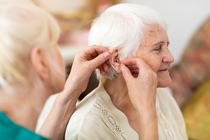 Female doctor applying hearing aid to senior woman's ear 