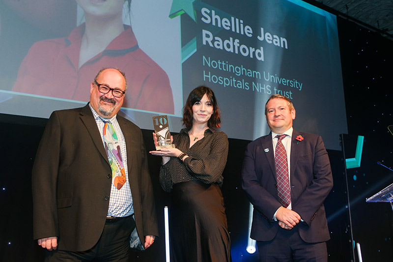 Shellie Jean Radford holding her award trophy on stage at the ceremony