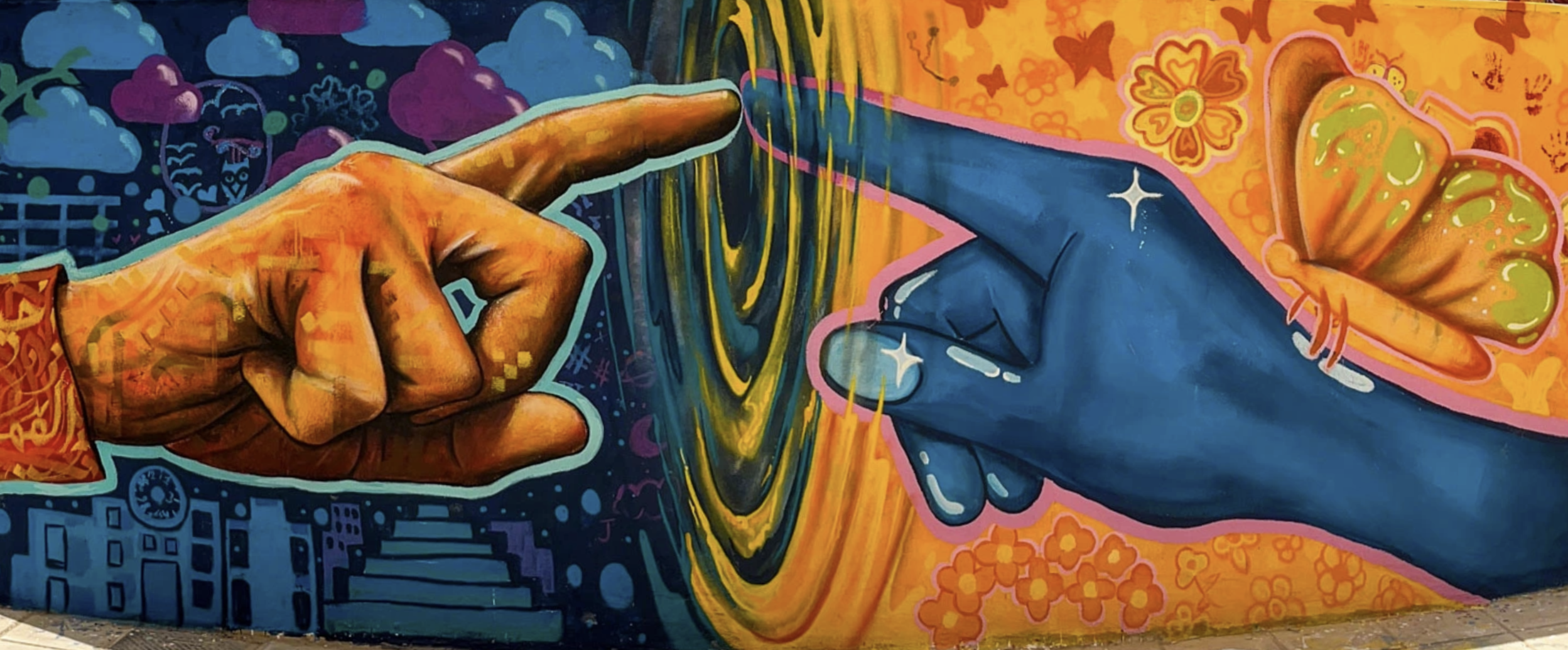 A mural painted on a wall showing two figures touching through a portal showing two distinct sides