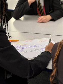 Three teenage school children discussing health issues and writing their thoughts on flip chart paper