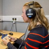 A young person takes part in hearing test research at a computer, using headphones and a controller with two buttons