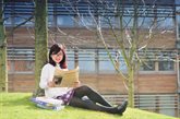 Female student sitting under a tree, reading a newspaper