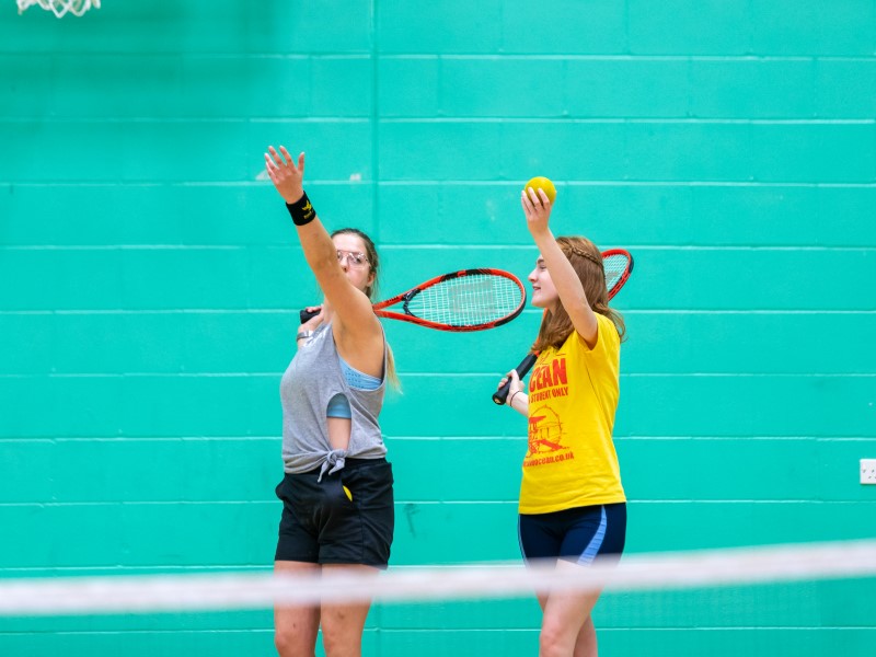 Female student demonstrates tennis serve to female student