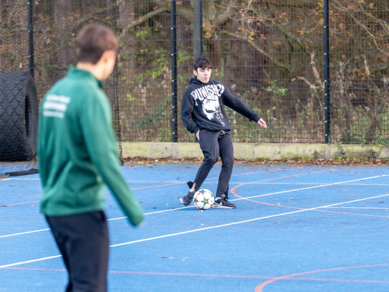 School pupil plays football with sports leader