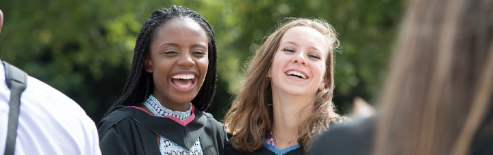 Two female students in graduation gowns smiling together