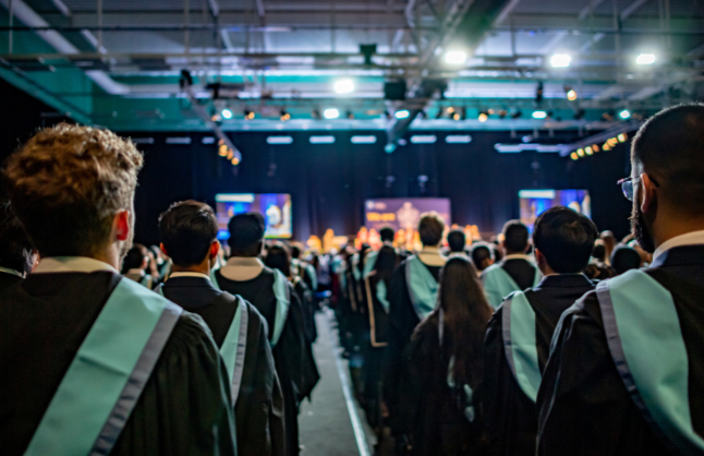 A photograph taken of behind a group of graduating students wearing their gowns during the graduation ceremony