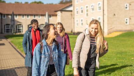 A group of smiling students walking past a university hall on campus
