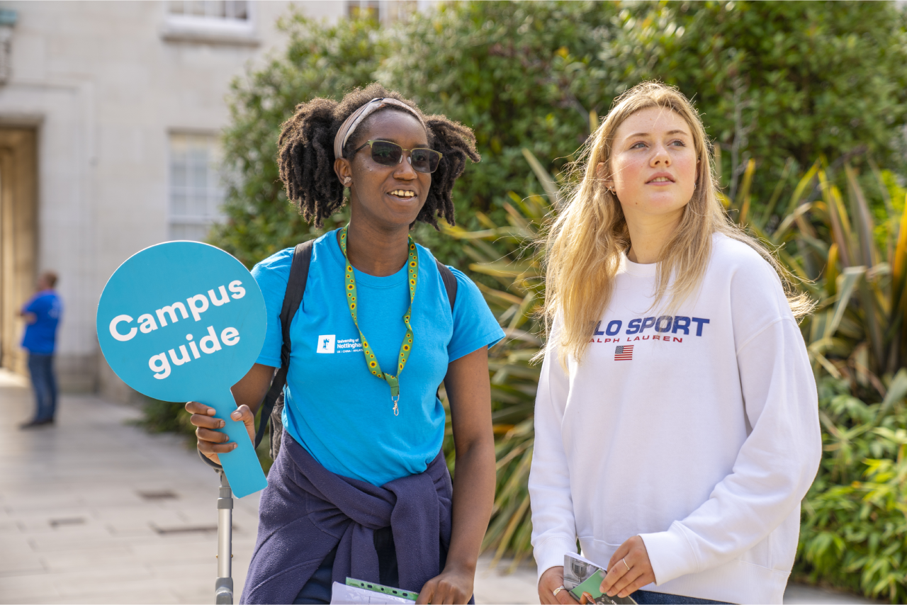 Student ambassador holding a sign saying 'Campus guide' talking to a visitor