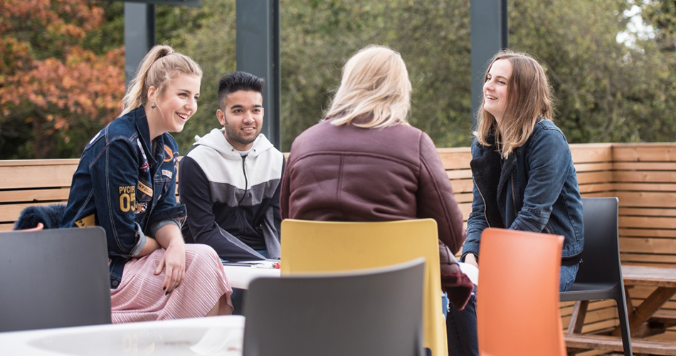 A group of students sat chatting at an outdoor table on one of our campuses