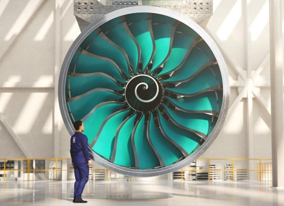 Researcher in blue overalls stands in front of a large aircraft turbine