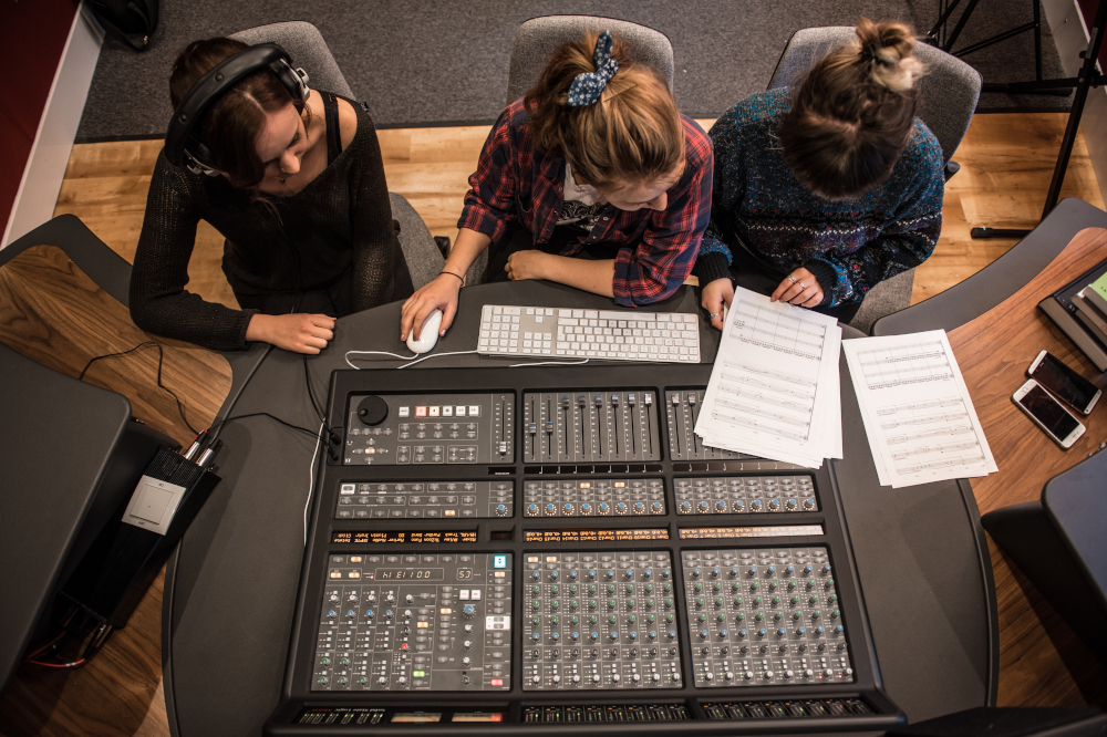 Overhead view of three students sitting at a mixing desk in a recording studio