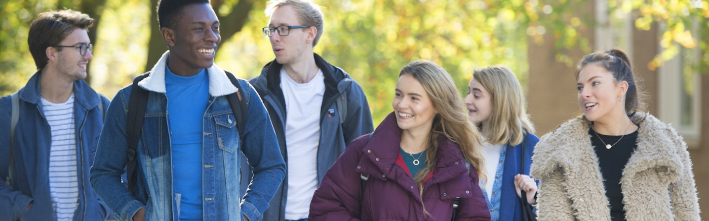 Mixed group of students walking underneath trees talking and laughing