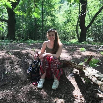 Maddi Maya sitting on a forest floor smiling
