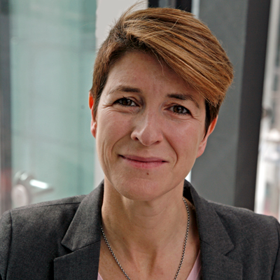 A professional headshot photo of Rachel Ashdown, wearing a grey blazer and smiling in front of a window