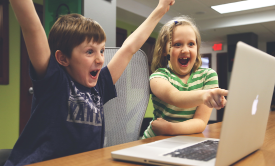 Two children looking excitedly at a laptop