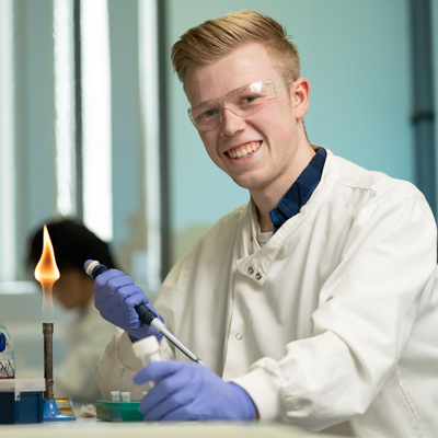Student smiling next to bunsen burner in a lab