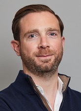 Head and shoulders photo of Jordan Buck. Jordan is wearing a white shirt and navy jacket and he has a short beard.