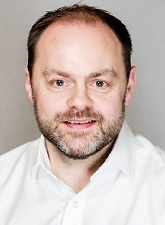 Head and shoulders photo of Mark Evans. Mark is wearing a white shirt and he is smiling and he has a short beard.