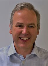 Head and shoulder photo of David Pemberton. David is smiling and is wearing a light coloured checked shirt. 